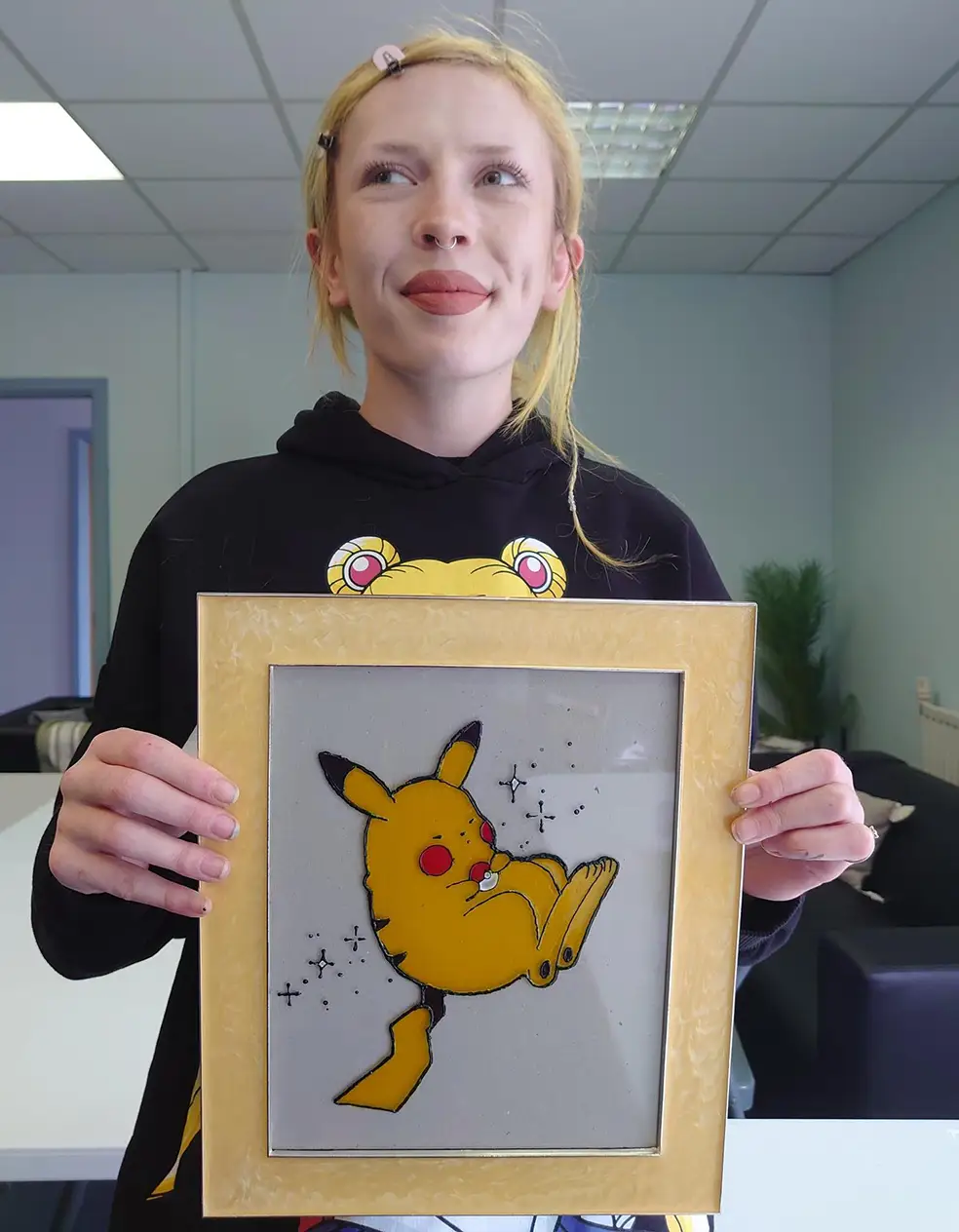 Person holding framed Pikachu artwork, smiling.