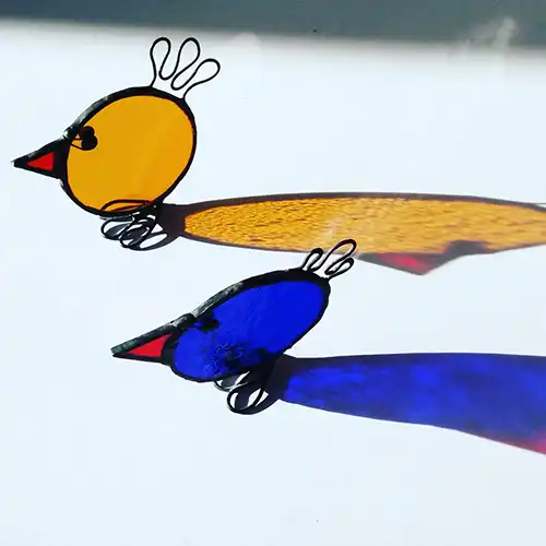 Colorful glass birds casting shadows on white surface.